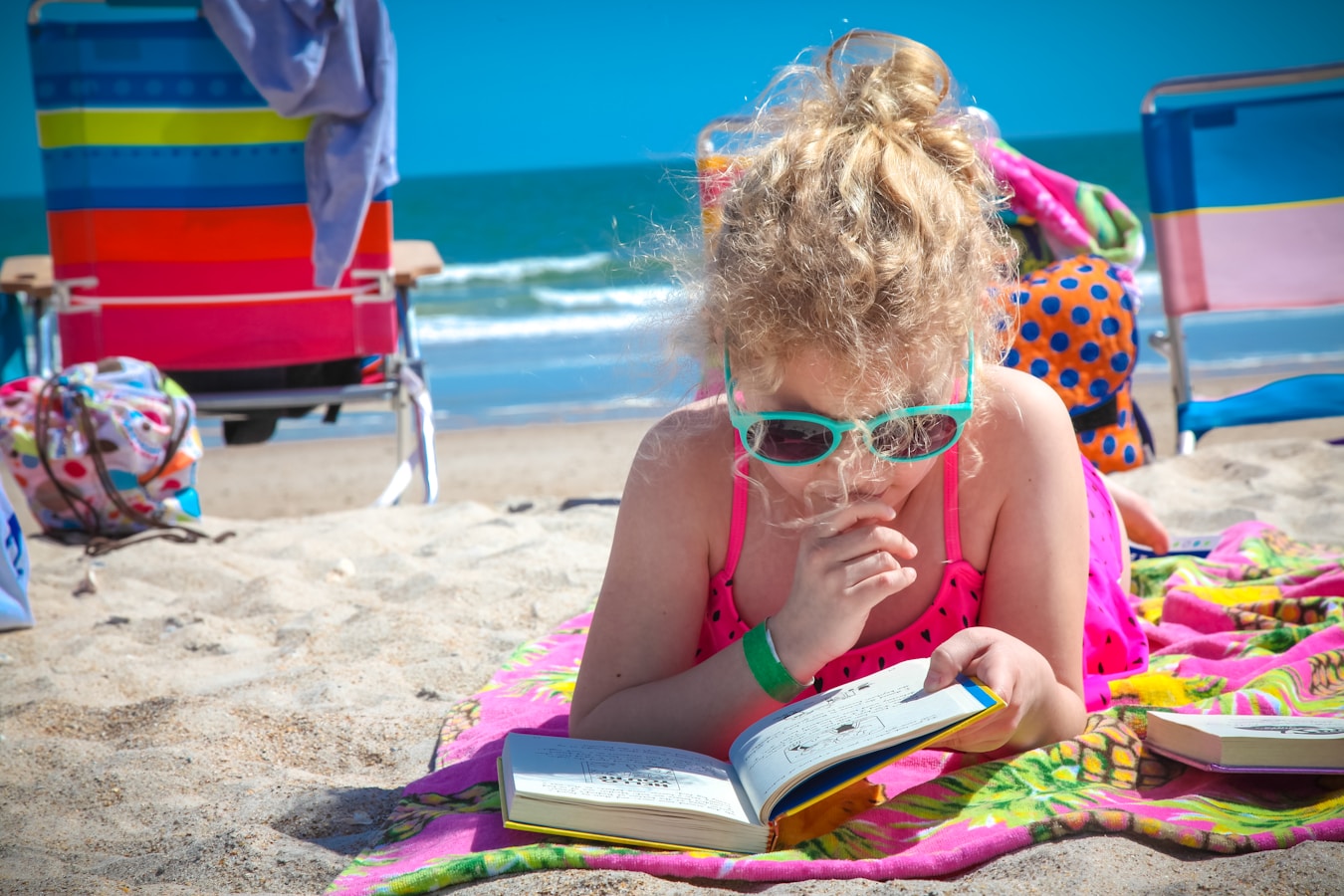 girl in pink tank top wearing eyeglasses reading book on beach during daytime from 10 Vacation Ready Book Series article