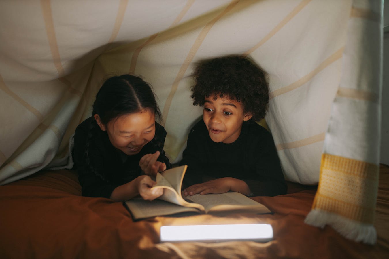 Two children read a book together under a cozy blanket fort, illuminated by soft lighting from Books Like Franklin the Turtle: 10 Best Read-Alike Series