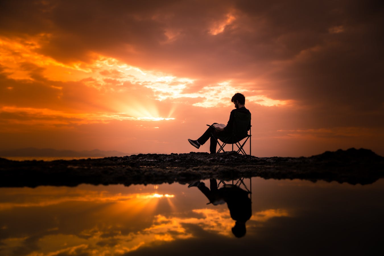 A person reading on a chair by a reflecting pond at sunset in Korgan, Turkey from 15 Reading Challenge Ideas for 2026 to Level Up Your Reading Life